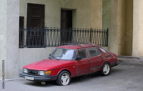 An old broken red car with a flat tire is parked against the wall of a house, Tallinskaya Street, St. Petersburg, Russia, June 2022 © Станислав Вершинин