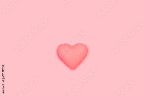 Un corazón rosa de tela hecho a mano sobre un fondo rosa liso y aislado. Vista superior y de cerca. Copy space