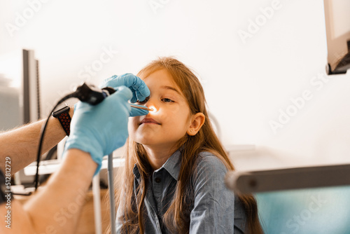 Nose endoscopy of child. Rhinoscopy procedure with rhinoscope. ENT doctor otolaryngologist with headlight treat nose kid patient.