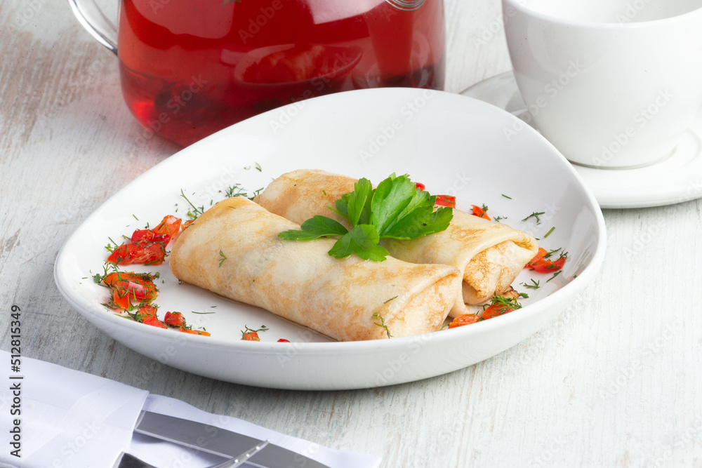 Traditional pancakes with filling, against the background of a teapot with red tea