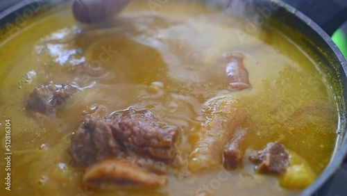 Handheld close up view of wooden ladle showing meat of steaming traditional Dominican creole food called Sancocho photo
