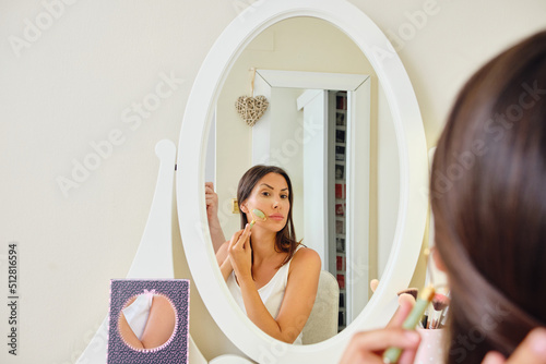 young beautiful woman in dressing room performing facial massage with jade roller