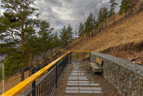 Empty tourist trail in rainy springtime day in the mountain hillside. Metal staircase with wooden railing among pine trees on Torgashinsky ridge in Krasnoyarsk  Russia