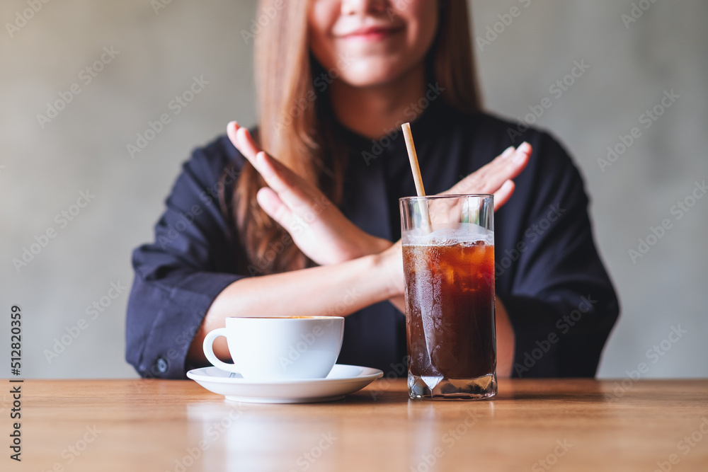 A young woman making arms crossed hand sign to refuse iced coffee and hot coffee A young woman making arms crossed hand sign to refuse iced coffee and hot coffee