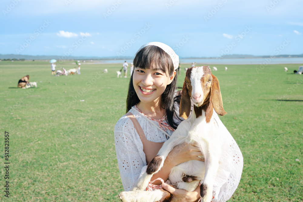 Portrait of a beautiful young woman with a Boer goat in grass field.Cute brunette holding a little goat