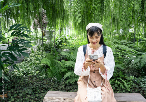 Fototapet Charming young Asian woman close-up in Green garden reads message to mobile phone, against green of summer park