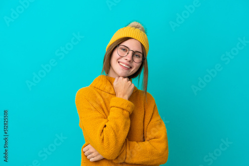 Young English woman wearing winter jacket isolated on blue background with glasses and smiling © luismolinero