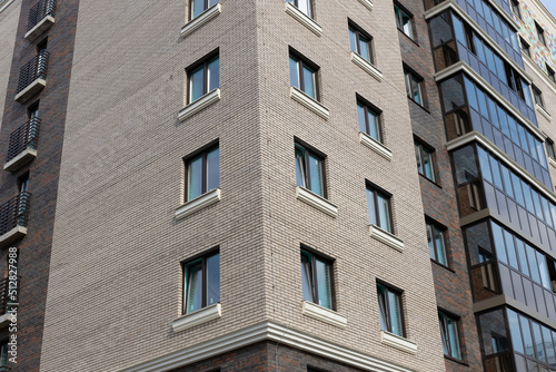 Corner of modern panel high-rise building with windows. Facing imitates a brick wall