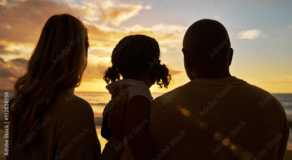 Silhouette closeup of happy family with one child on the beach looking at view at sunset. Two parents and daughter admiring golden sky and calm sea while enjoying their vacation and spending time