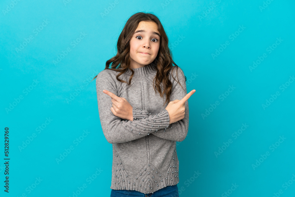 Little caucasian girl isolated on blue background pointing to the laterals having doubts