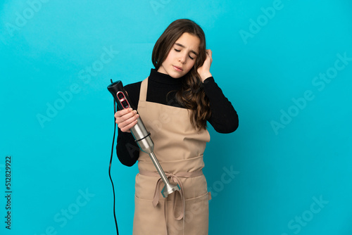 Little girl using hand blender isolated on blue background with headache
