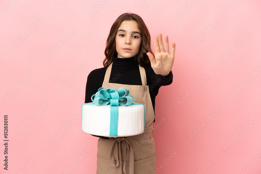 Little Pastry chef holding a big cake isolated on pink background making stop gesture Little Pastry chef holding a big cake isolated on pink background making stop gesture