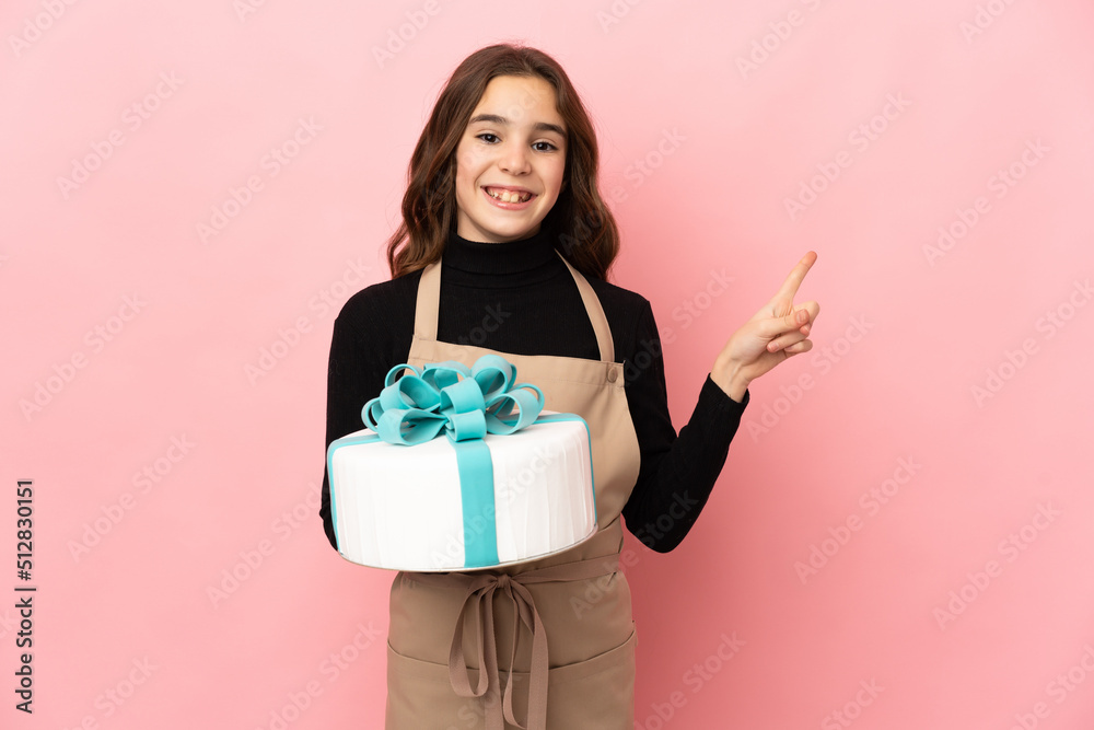 Little Pastry chef holding a big cake isolated on pink background pointing to the side to present a product Little Pastry chef holding a big cake isolated on pink background pointing to the side to present a product