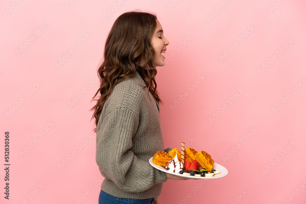 Little girl holding waffles isolated on pink background laughing in lateral position Little girl holding waffles isolated on pink background laughing in lateral position