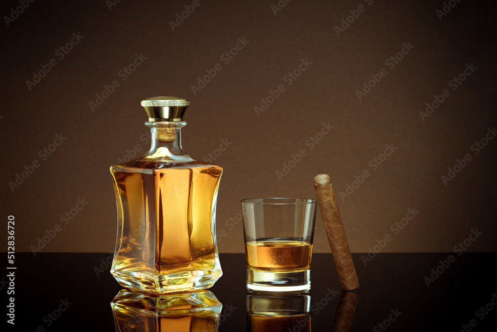 close up view of cigar, bottle of whiskey and glass aside on color back. close up view of cigar, bottle of whiskey and glass aside on color back.