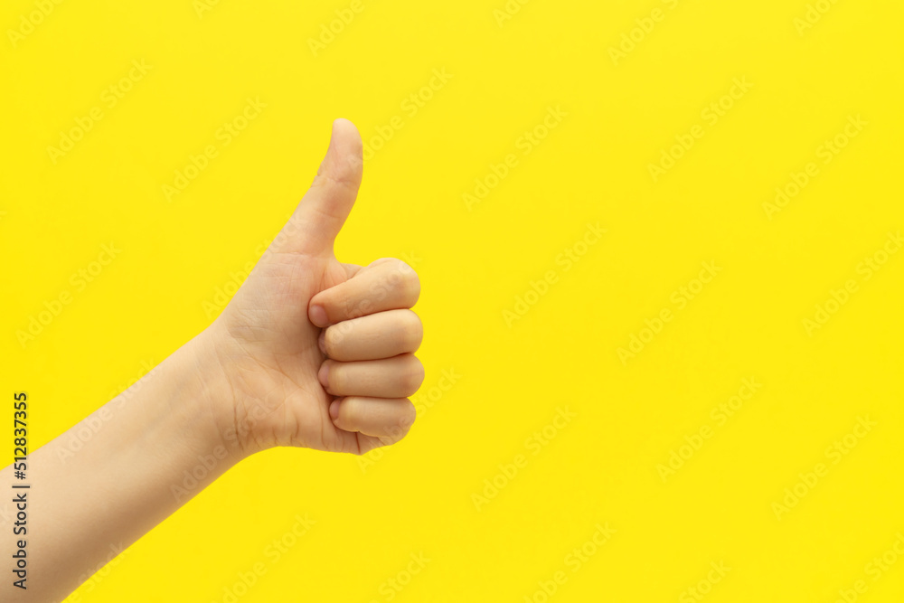 Child hand with satisfacting thumb up gesture on vivid yellow background.