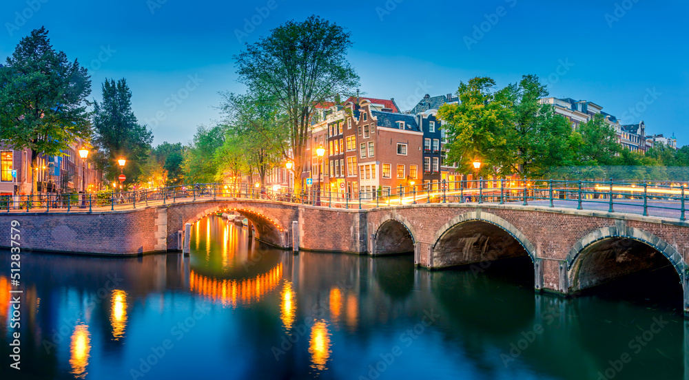 Romantic Amsterdam lit the lights. Evening panoramic view of the famous historic center with lantern lights, bridges, canals and cute Dutch houses.