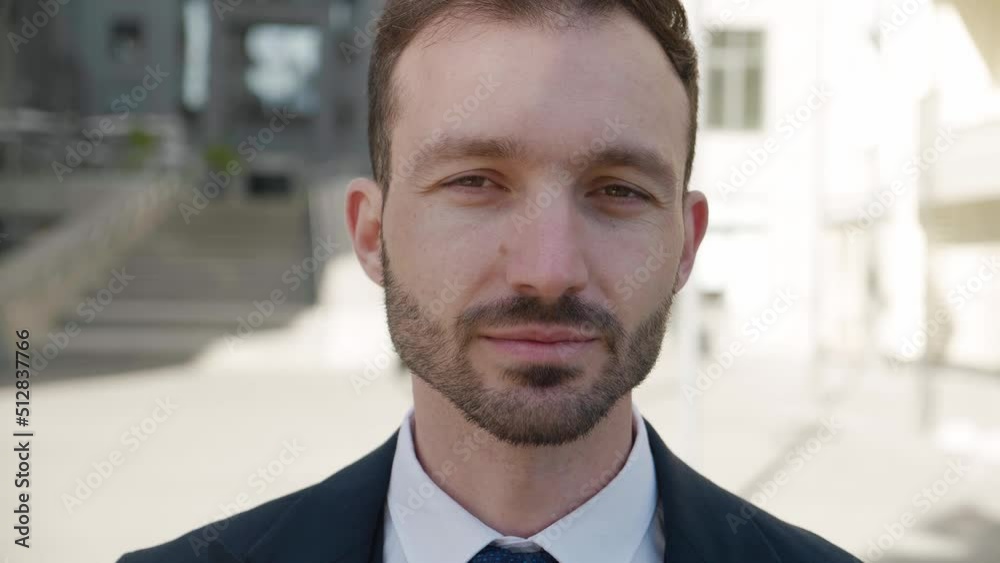 Close-up portrait of smiling ceo executive looking to camera. Male businessman in 30s wearing classical suit posing outdoors on modern office building background Close-up portrait of smiling ceo executive looking to camera. Male businessman in 30s wearing classical suit posing outdoors on modern office building background