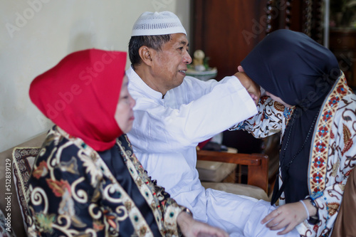 Portrait of young muslim woman kneeling and kiss her parent's hand asking for forgivness. Indonesian traditional gesture called sungkem. Eid mubarak, ramadan, idul fitri day concept.  photo