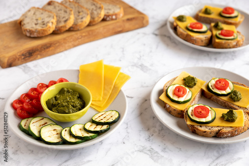Open sandwiches with bread, cheese slices, grilled zucchini, tomato and coriander chutney and ingredients to prepare.