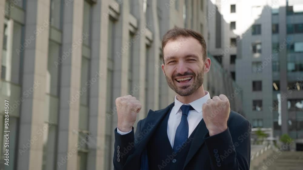 Amazed european businessman winner celebrating success win, surprised to camera, standing at business district. Happy male manager in formal suit showing Yes winner gesture. Victory concept. Amazed european businessman winner celebrating success win, surprised to camera, standing at business district. Happy male manager in formal suit showing Yes winner gesture. Victory concept.