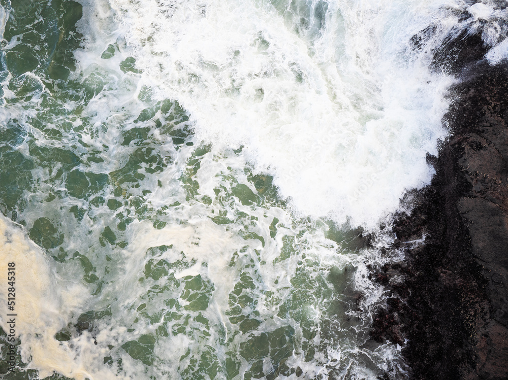 Top view of the raging ocean. White foamy waves crash against the shore. Abstraction. Minimalism. Wildlife beauty, environmental protection, geology, weather, extreme sports.