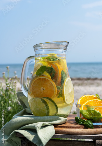 Detox infused water with lime, oranges, mint on the beach with sea coast view