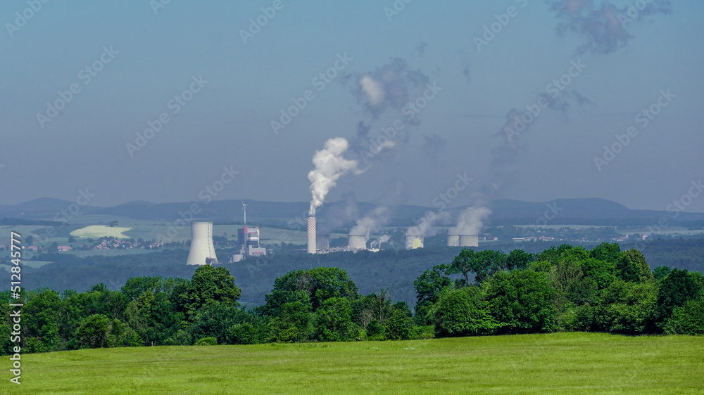 Chimneys of carbon power plant emitting carbon dioxide to the air in the background of the forest trees