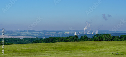Panoramic view of meadow and forest with coal and wind power energy plants in background
