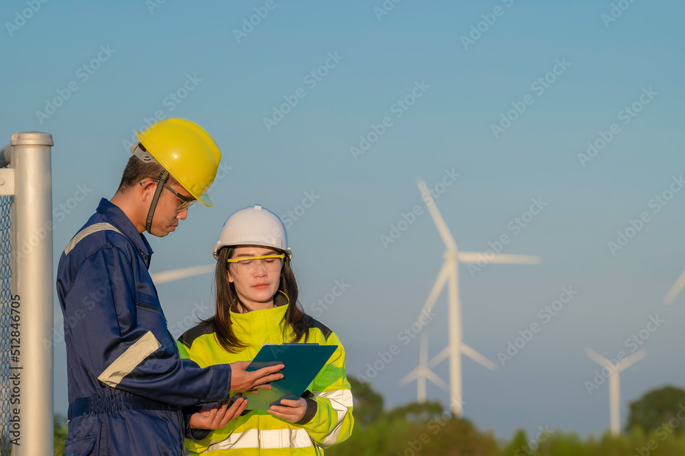 Two engineers working and holding the report at wind turbine farm Power Generator Station on mountain,Thailand people,Technician man and woman discuss about work Two engineers working and holding the report at wind turbine farm Power Generator Station on mountain,Thailand people,Technician man and woman discuss about work