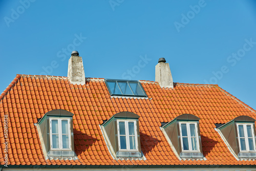 Chimney chutes, windows and sunroof skylight designed on house building outside against blue sky background. Construction of exterior architecture on rooftop for fireplace escape and natural sunlight photo