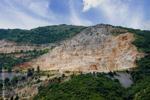 Natural quarry is located near road against backdrop of Rhodope Mountains and hills with forests and mountain vegetation