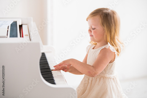 A little baby plays a big white piano in a bright sunny room