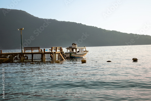 Lonely fishing boat moored at a wooden pier facing the horizon on calm waters in the late afternoon. Maguariquessaba Beach, Ilha Grande, Angra dos Reis, Rio de Janeiro, Brazil. photo