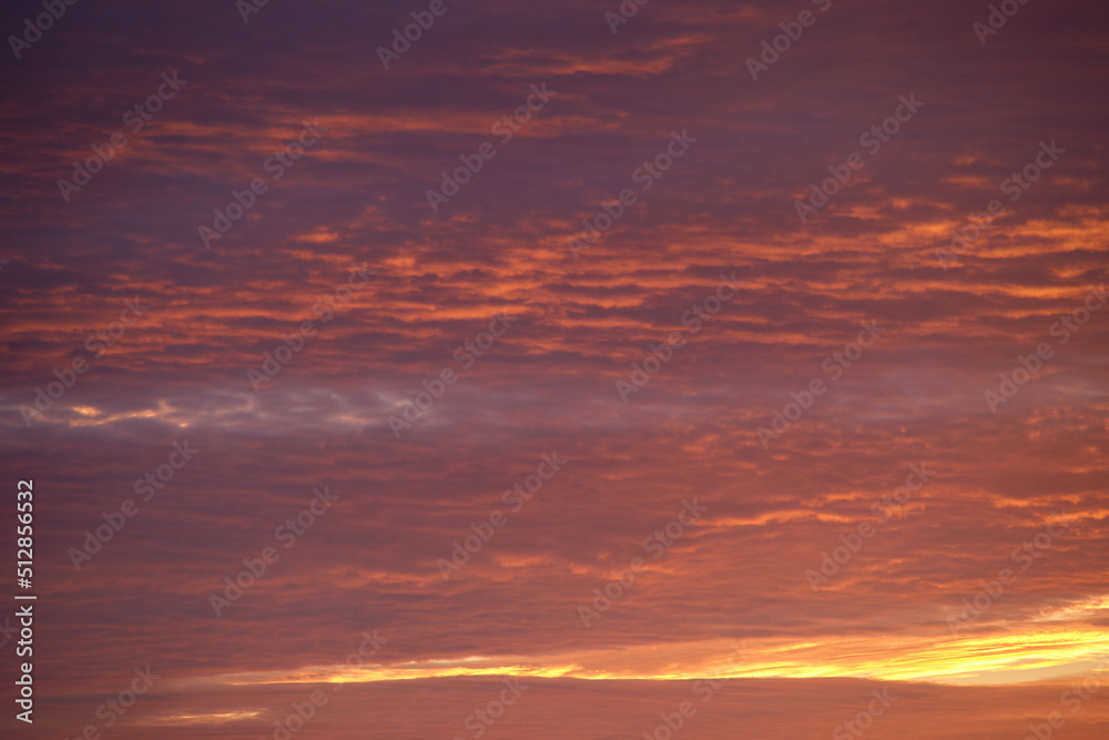 Bright colorful sunset sky with vivid smooth clouds illuminated with setting sun light spreading to horizon