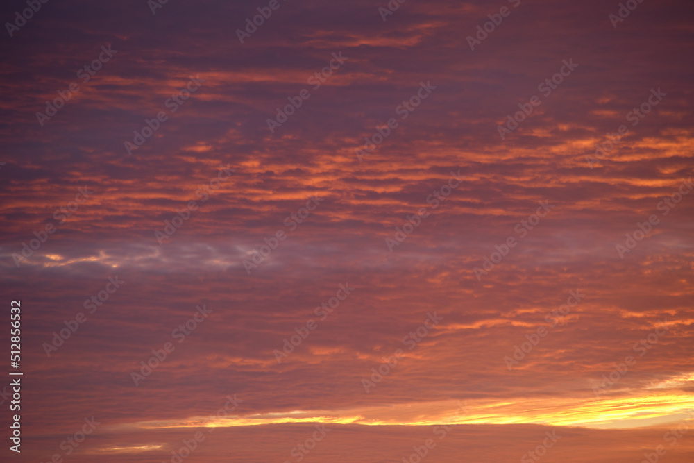 Bright colorful sunset sky with vivid smooth clouds illuminated with setting sun light spreading to horizon Bright colorful sunset sky with vivid smooth clouds illuminated with setting sun light spreading to horizon