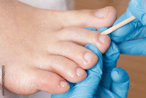 pedicure master processes the cuticle on the toes with a wooden stick