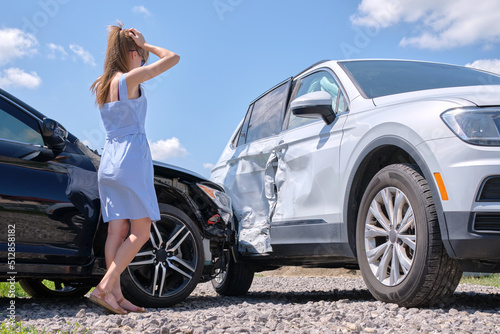Canvas Print Sad young woman driver standing near her smashed car looking shocked on crashed