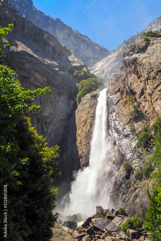 Vertical shot of Lower Yosemite Fall on a beautiful sunny summer day, Epic waterfall under blue sky in Yosemite National Park, California, USA. Natural wonders of the world.