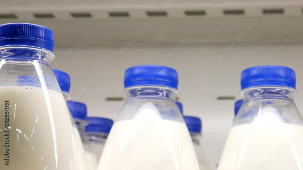 Close-up of many plastic milk bottles with blue caps and a male buyer's hand takes one Close-up of many plastic milk bottles with blue caps and a male buyer's hand takes one