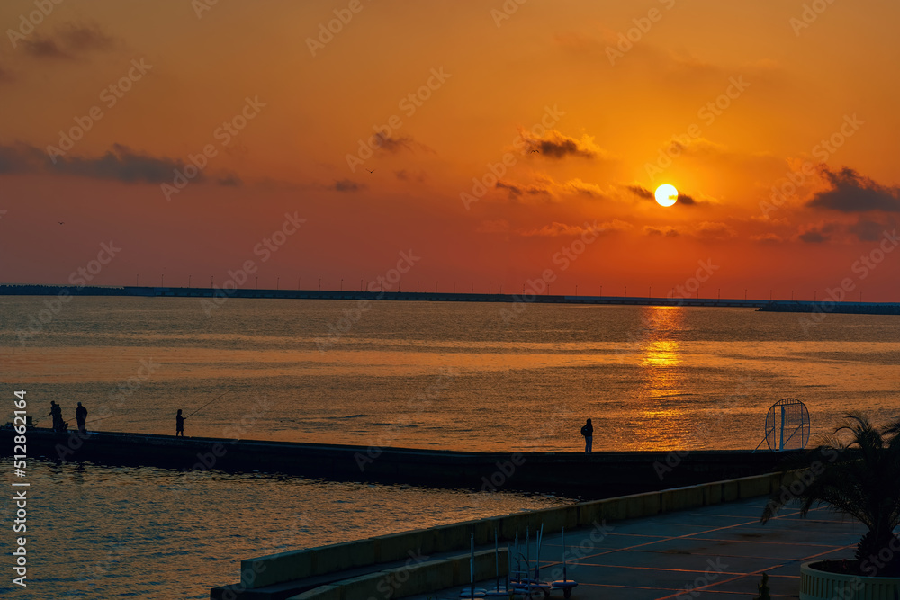View of the setting sun and the Sochi embankment. Pier in the colors of the setting sun. Sunset over Black Sea