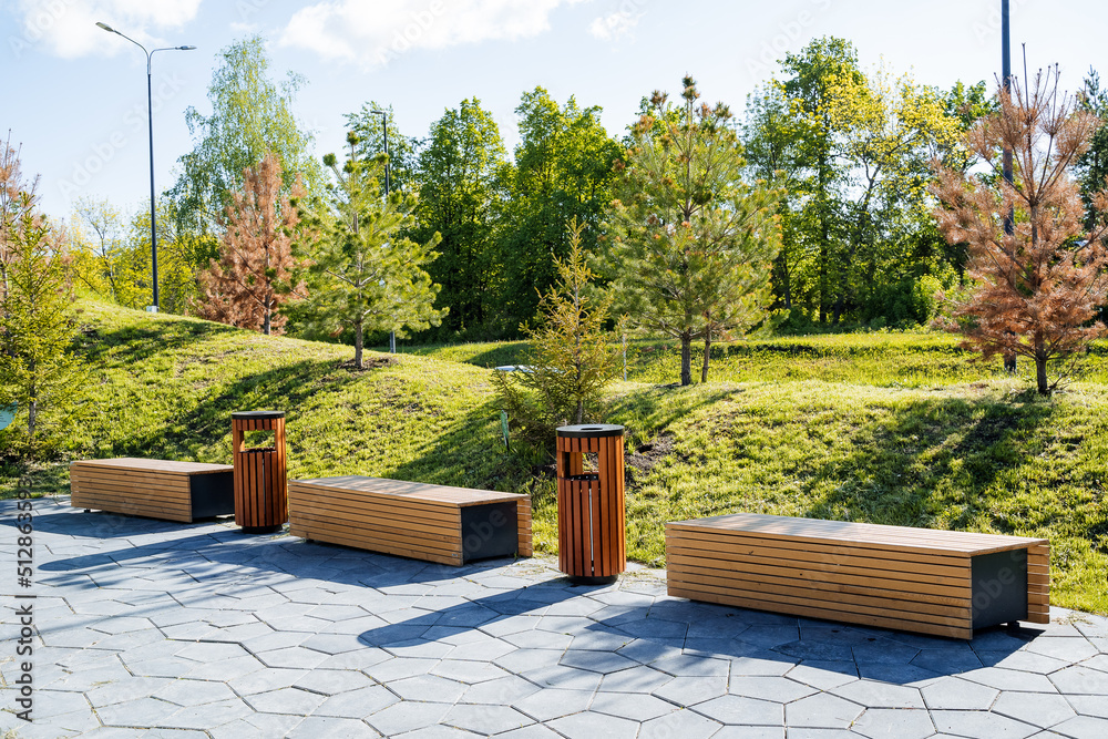 Beautiful landscape design of the city park, a pleasant place for walks and recreation of citizens, wooden benches for sitting, a sidewalk in the park. - obrazy, fototapety, plakaty 