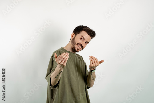 Caucasian young man wearing t-shirt posing isolated over white background inviting to come closer with hands. Happy that you came.