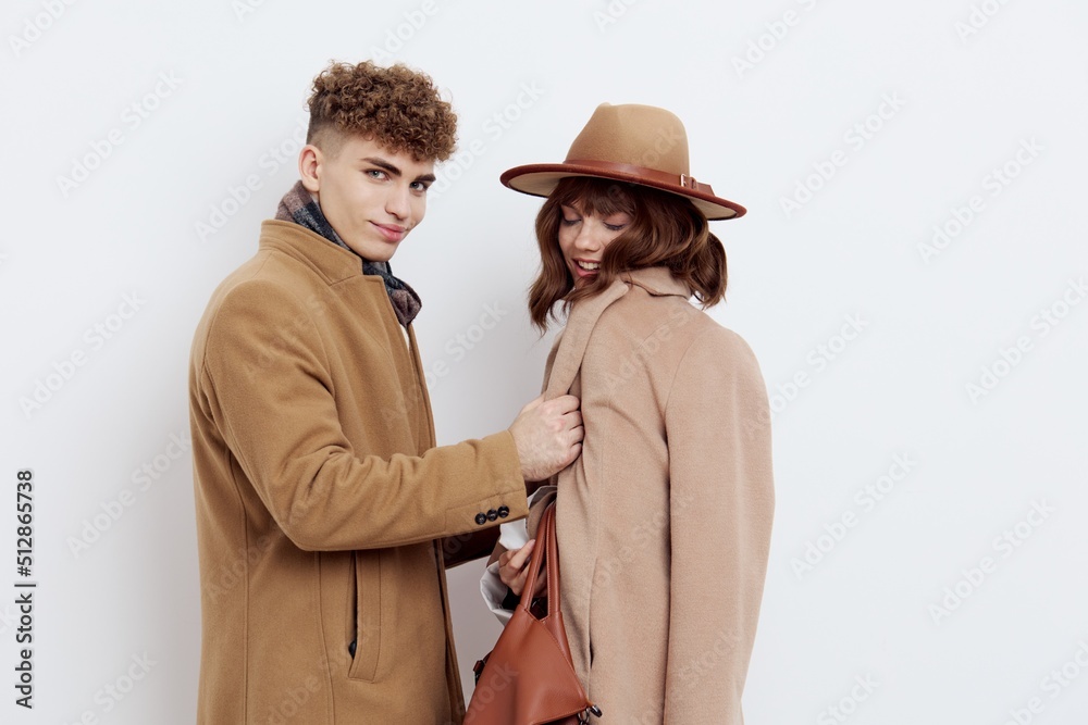 a man helps a woman to fasten her stylish brown coat, standing on a white background and looking at her with love a man helps a woman to fasten her stylish brown coat, standing on a white background and looking at her with love