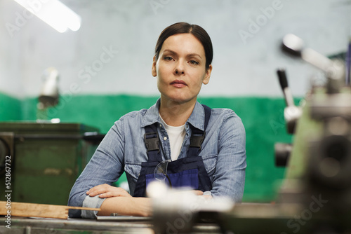 Photography Portrait of serious tenacious lady engineer with brown hair leaning on table at