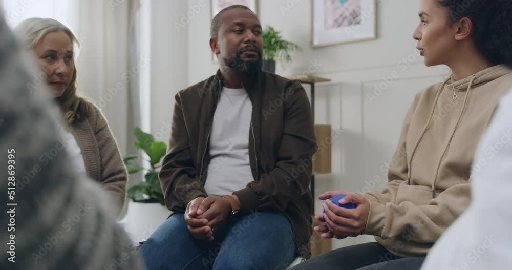 Closeup of a support group of diverse people passing a blue ball and talking during a group therapy session while sitting in a circle. A variety of men and women sharing their problems in therapy