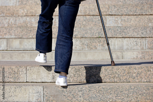 Woman wearing jeans with walking cane climbing stairs outdoor, legs in motion on the street steps. Concept for disability, limping adult, diseases of the spine, old people photo