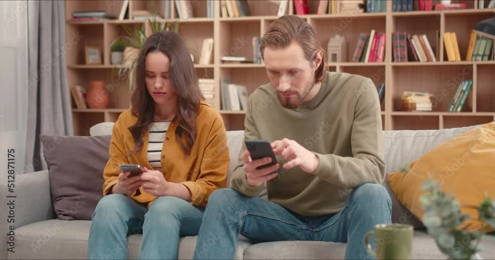 Close up on caucasian male and female sitting on couch scrolling phones. People ignoring communication while chatting in social media. Staying home during covid 19, quarantine concept. Close up on caucasian male and female sitting on couch scrolling phones. People ignoring communication while chatting in social media. Staying home during covid 19, quarantine concept.