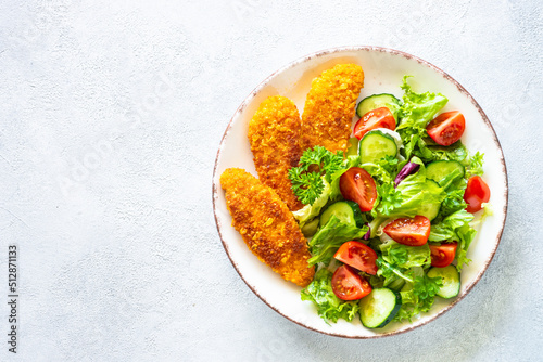 Chicken nuggets with fresh salad at white table.