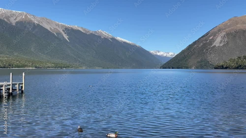 Snow capped mountain peaks and blue lake with ducks swimming close to a pier Snow capped mountain peaks and blue lake with ducks swimming close to a pier